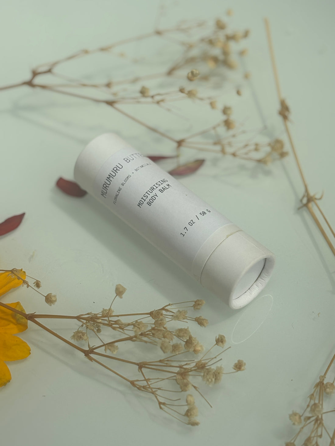 White cylindrical product with text on a light green surface with dried flowers