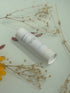 White cylindrical product with text on a light green surface with dried flowers